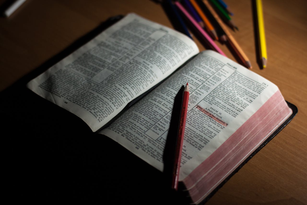 An open Bible on a wooden table accompanied by colored pencils, symbolizing study and spirituality.